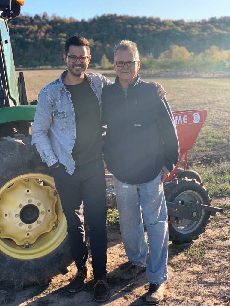 Two generations of the family together in the field beside a green tractor at golden hour
